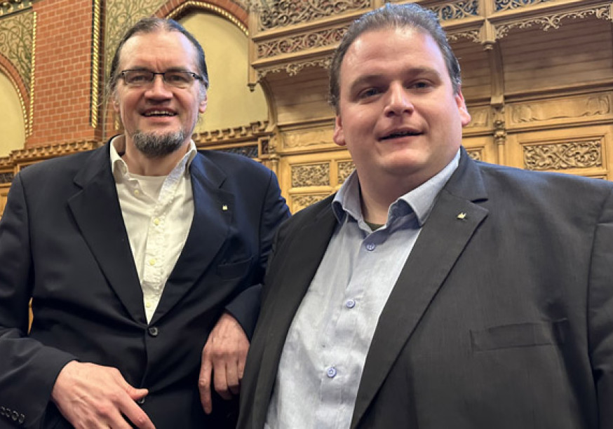 Tim Stüttgen und Gregor Voht stehen lächelnd im Lübecker Bürgerschaftssaal.