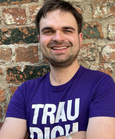 Martin Janßen steht im Volt T-Shirt vor einer Backsteinmauer.