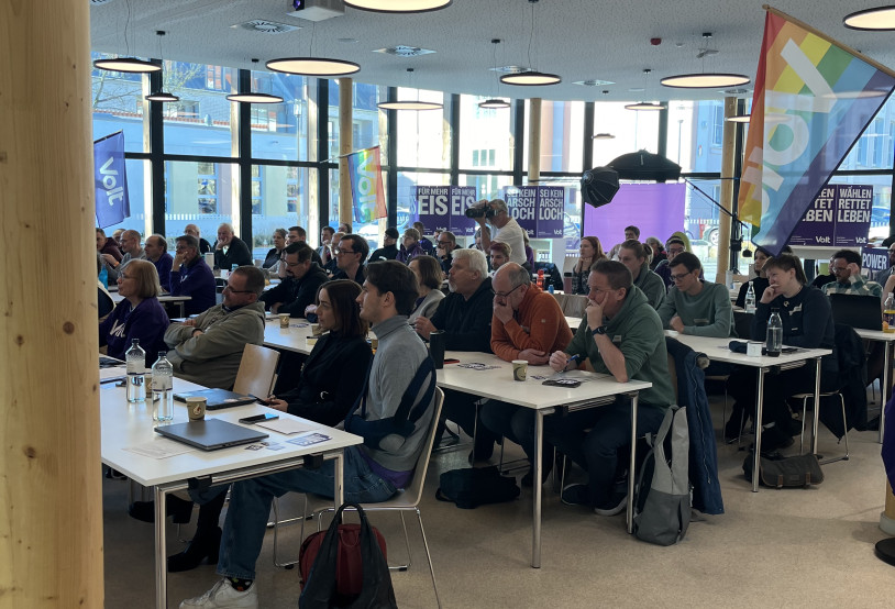 Die Mitglieder von Volt sitzen für den parteitag an Tischen.