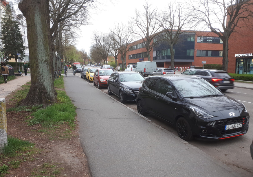 Ein Bild der Falkenstraße und des Radweg, mit Autos welche eine Spur zuparken.