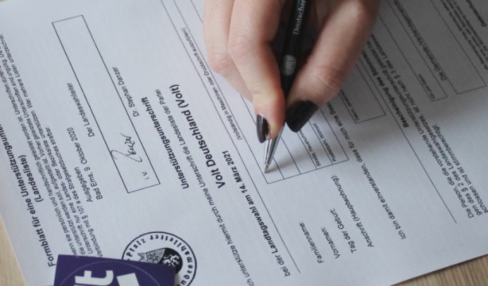 Foto eines Formulars, auf dem gerade eine Hand mit Stift eine Unterschrift setzt